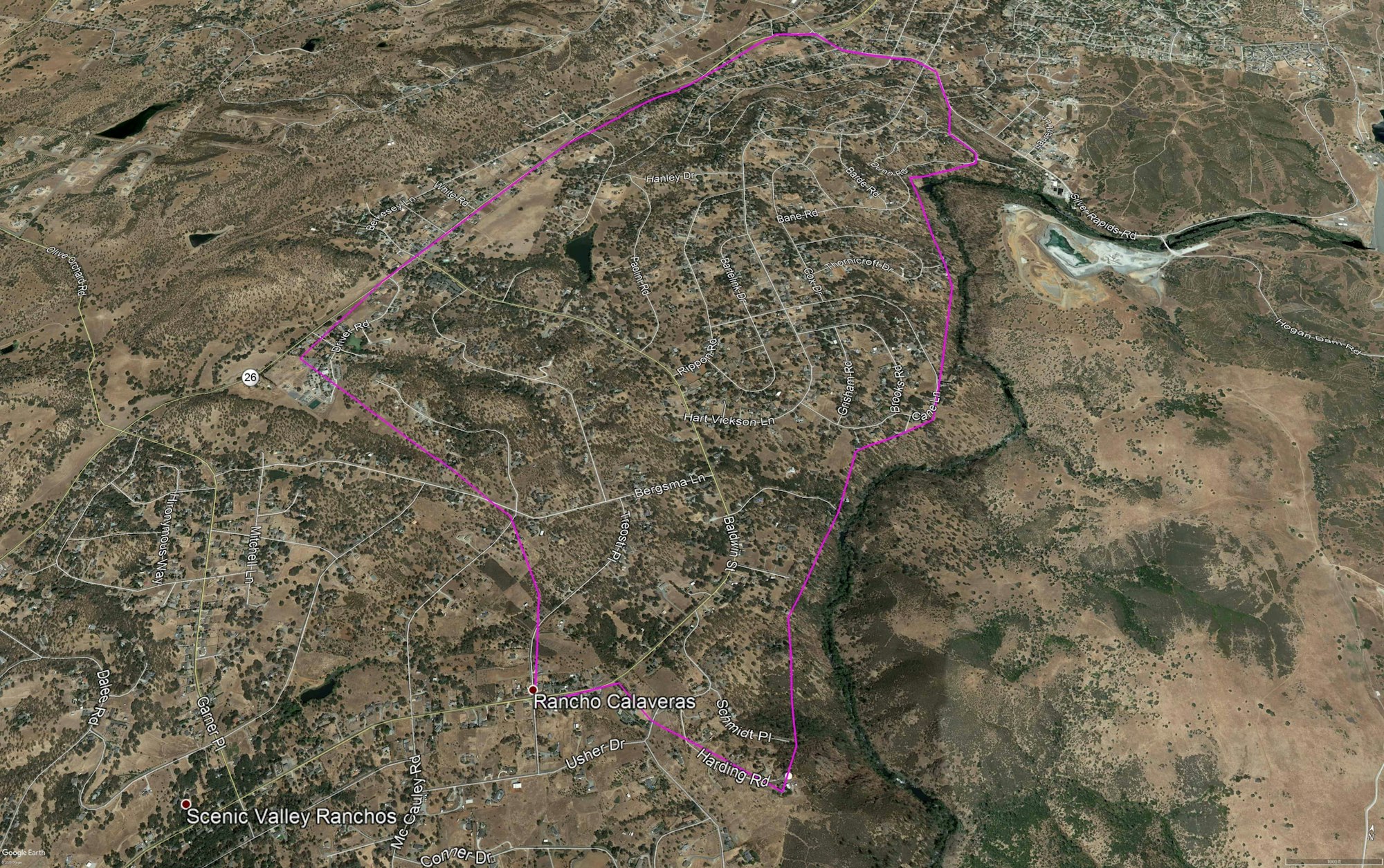 Satellite view showing a hilly terrain with roads and housing, outlined area possibly indicating a neighborhood or zone.