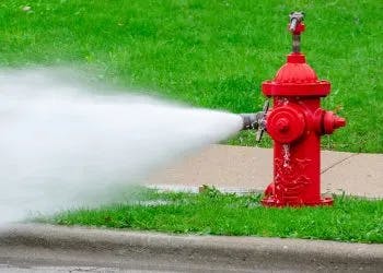 A red fire hydrant spraying water onto a street.