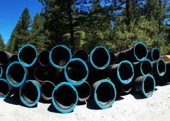 A stack of large black pipes with blue lining in a forested area.
