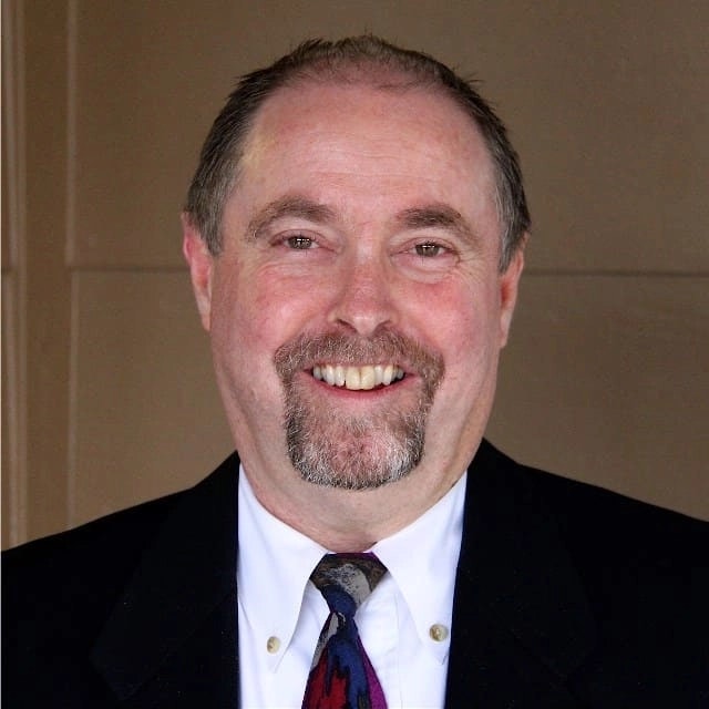 A smiling man with a beard, wearing a suit and tie.