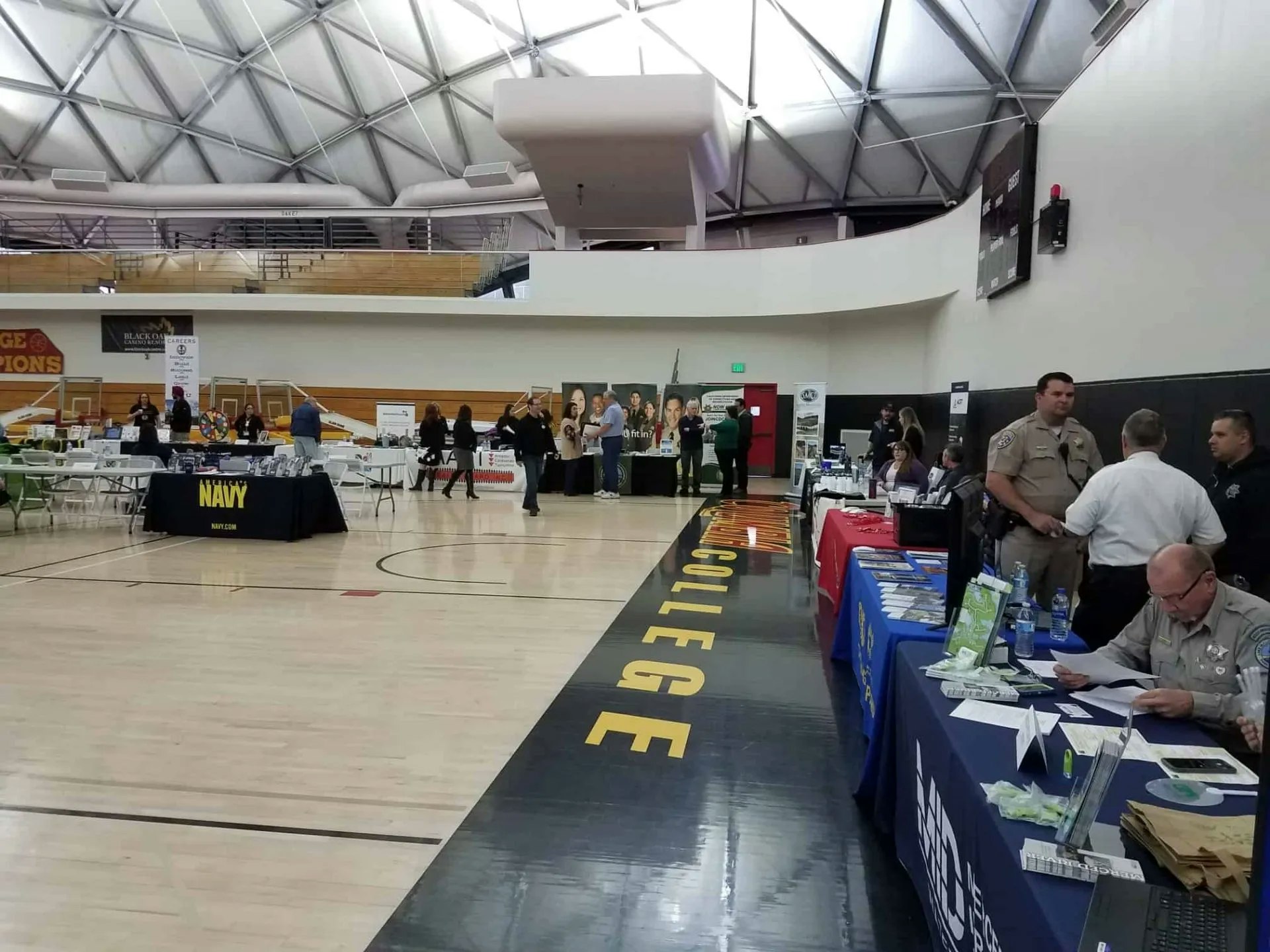 A career fair in a gymnasium with various booths, including military and law enforcement representatives.