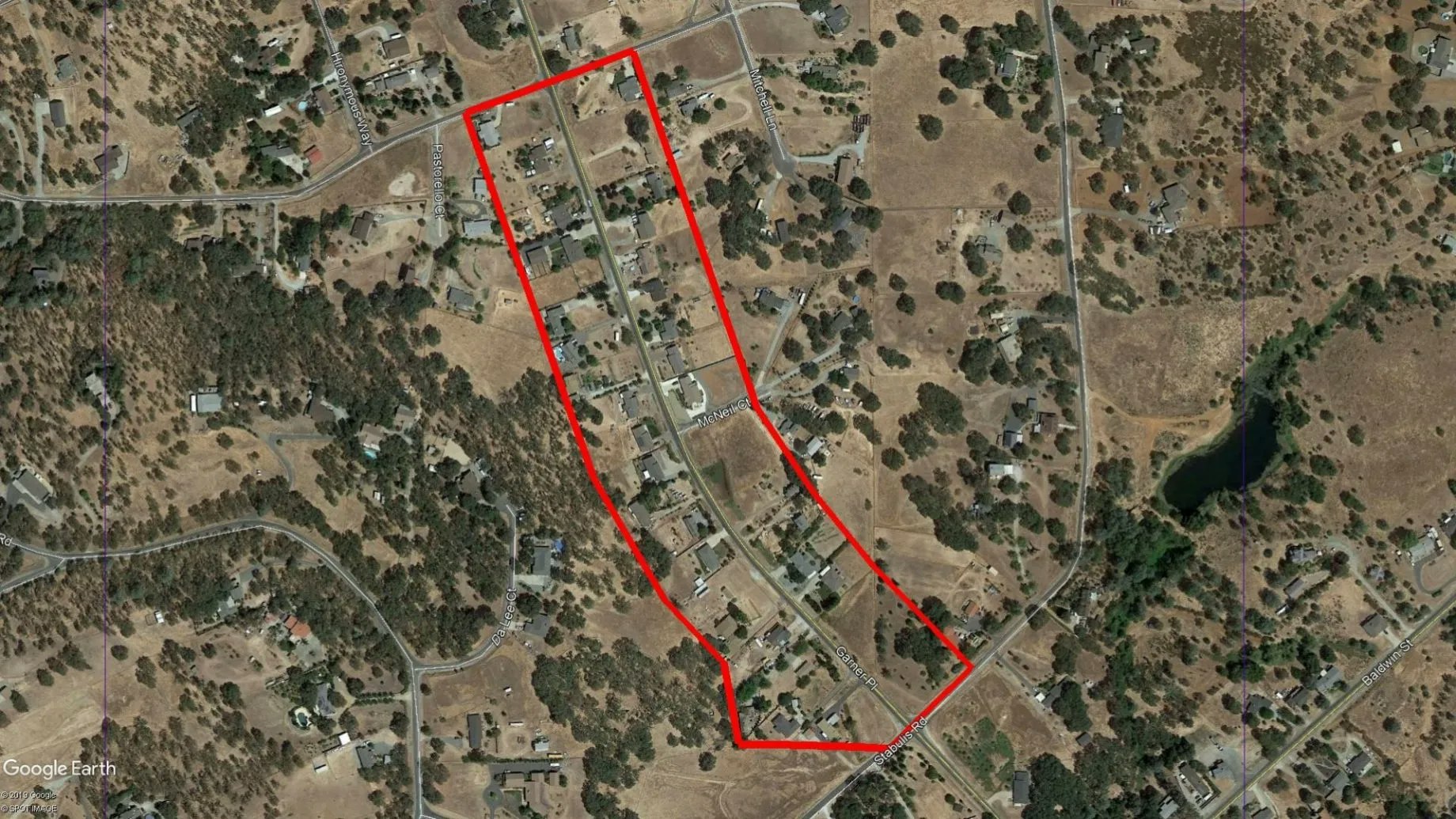 Aerial view of a rural area with a red outline, houses, trees, and roads visible.