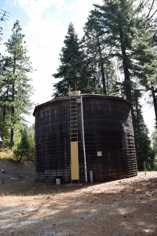 A large wooden water tank with a ladder, surrounded by trees.