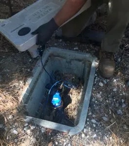 A person is installing or checking a water meter in an underground box.