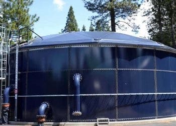 A large outdoor water storage tank surrounded by trees under a clear sky.