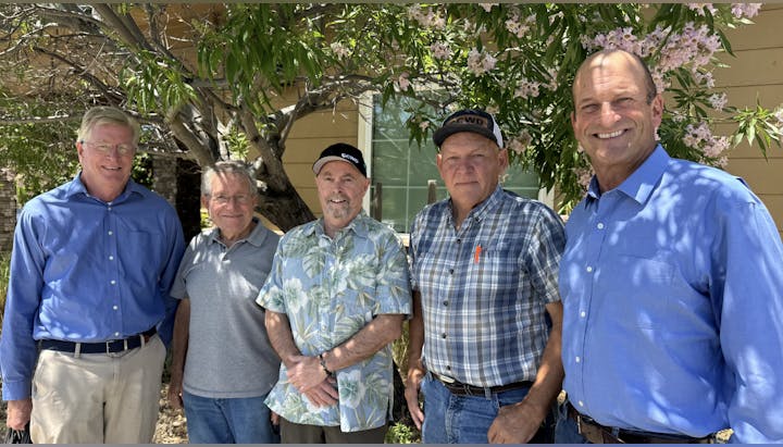 Five men standing outside, smiling, under a flowering tree.