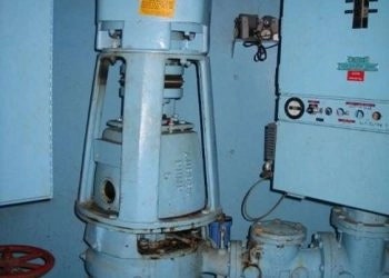Industrial machinery, possibly a pump or motor, with pipes and valves, inside a room.