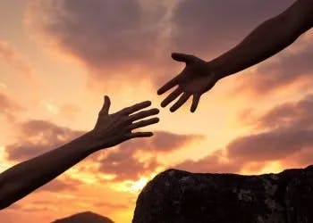 Two hands reaching towards each other against a sunset sky.