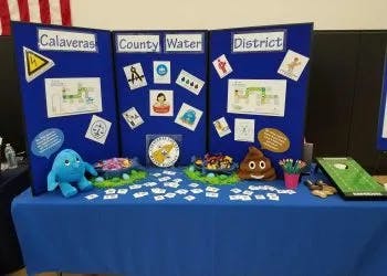 Exhibition booth with informational posters about water, plush toys, and handouts on a table.
