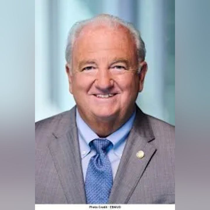 A smiling man in a suit with a tie, with a badge on his lapel. "Photo Credit: ERAU" is at the bottom.
