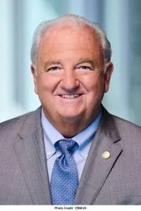 A smiling man in a suit with a tie, with a badge on his lapel. "Photo Credit: ERAU" is at the bottom.