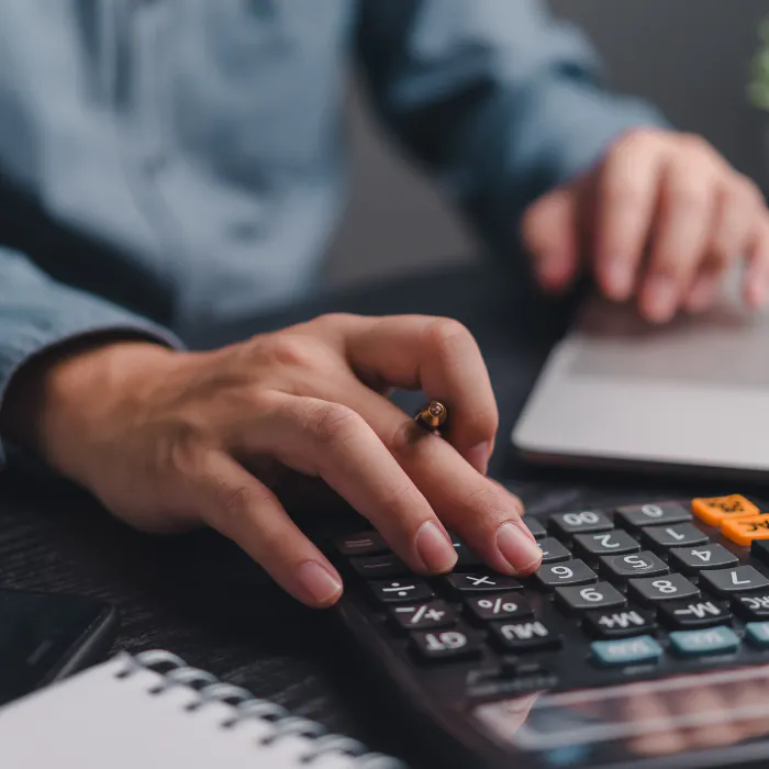 Person using a calculator and laptop, likely doing financial work.