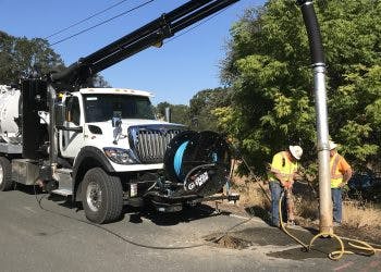 A vacuum truck and workers cleaning a street.