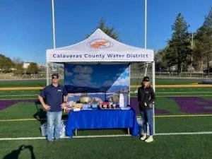 Two people at a Calaveras County Water District booth with a display table and a banner.
