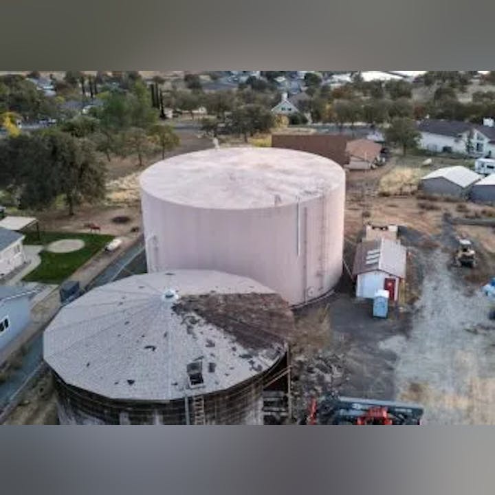 Aerial view of a large water storage tank next to a construction site with equipment, in a residential area.