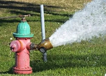 A fire hydrant spraying water onto grass.