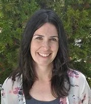 A smiling woman with dark hair, wearing a floral shirt, with greenery in the background.
