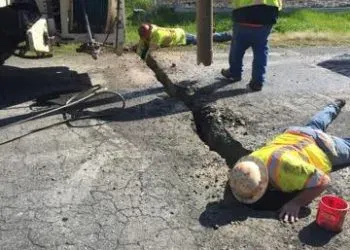 Workers mimicking a "crime scene" with a fake chalk line, humorously playing dead on a cracked road.