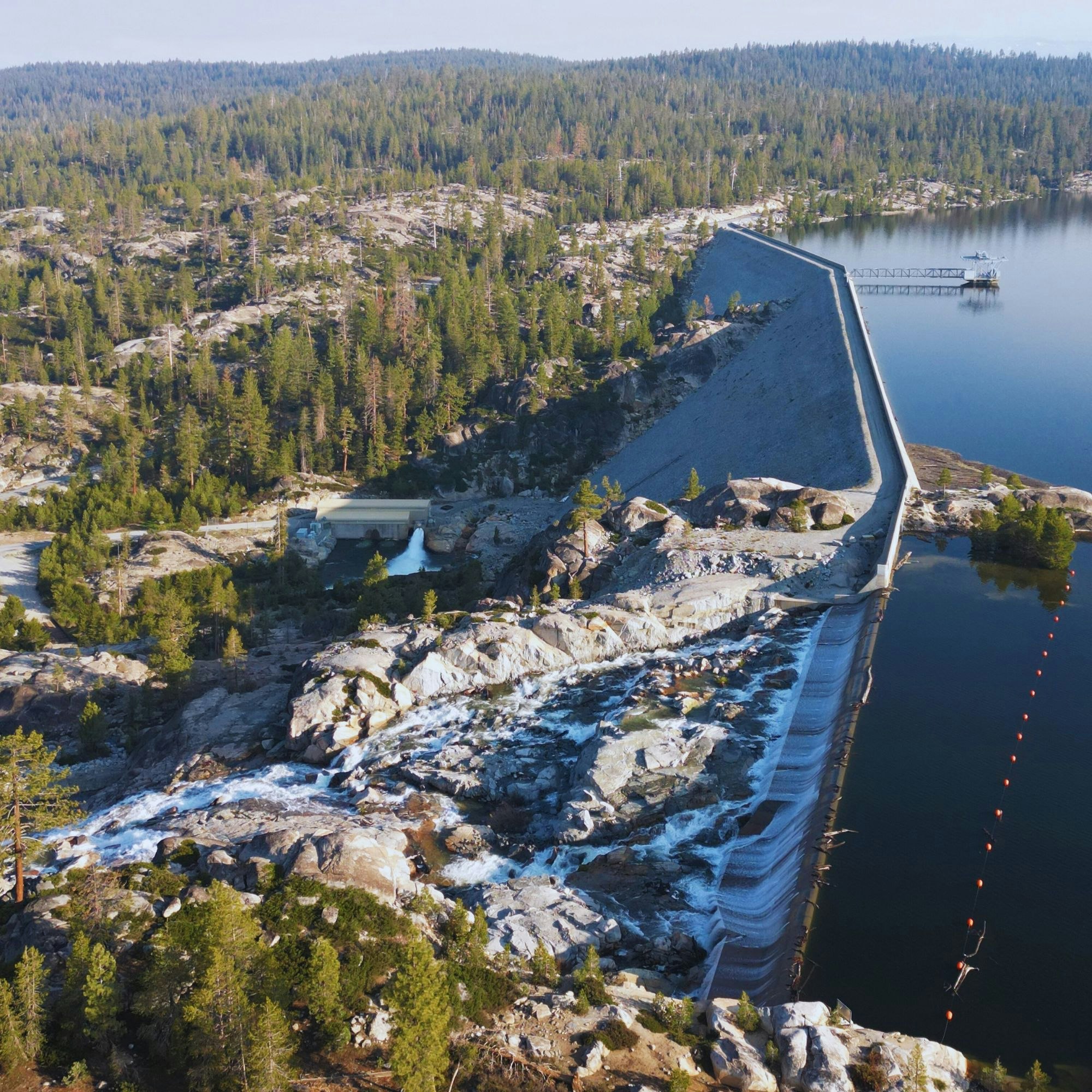 A dam with water flowing over rocks, surrounded by a forested landscape.