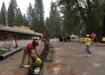 Workers and construction equipment on a road with wet conditions.