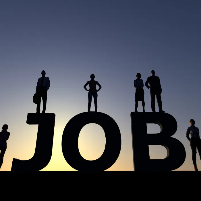 Silhouetted people standing on letters forming the word "JOB" against a dusk sky.