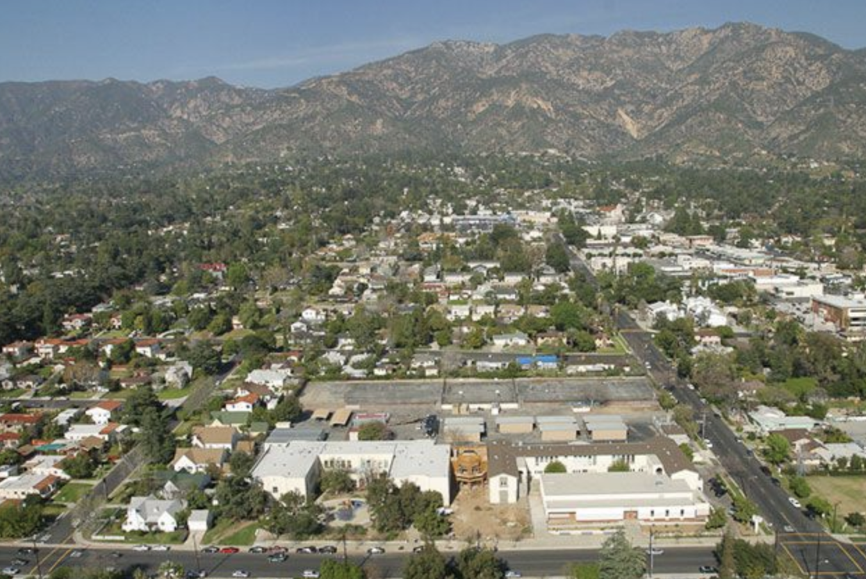 Aerial view of a suburban area with houses, roads, and a backdrop of mountains.