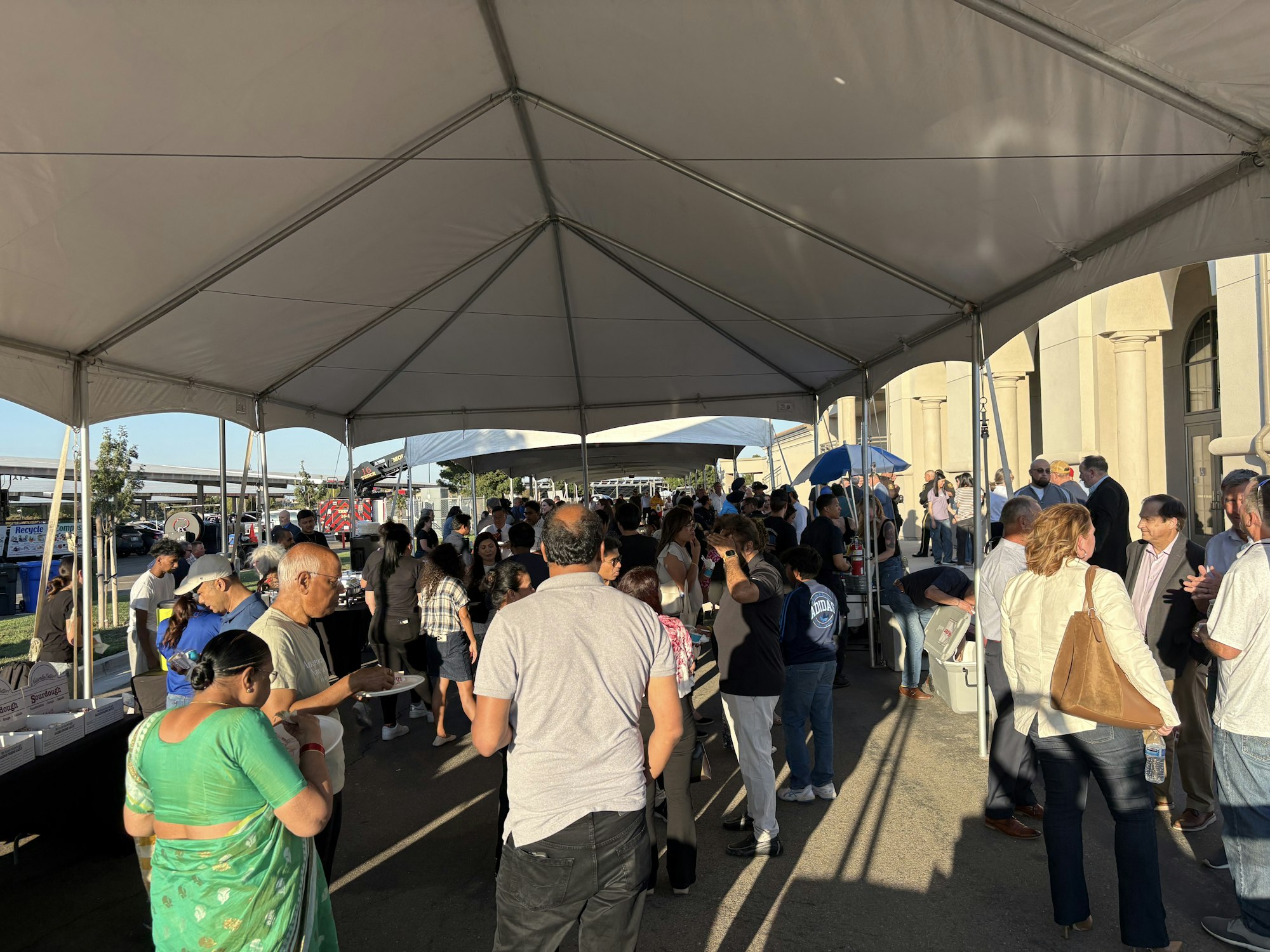 A large crowd of people gathered under a tent, socializing and eating.