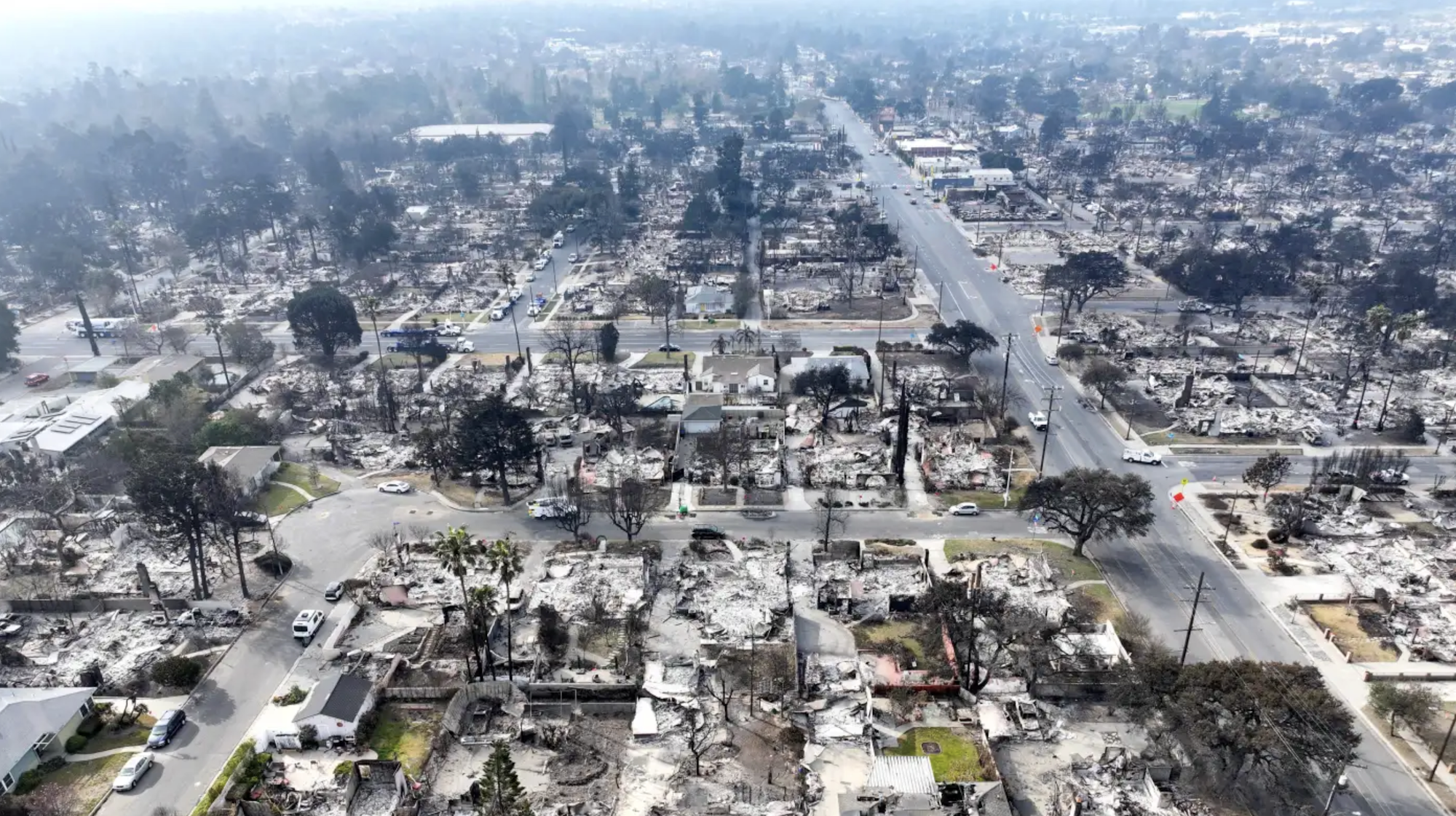 Aerial view of Altadena CA with extensive fire damage; burned structures and smoke visible.
