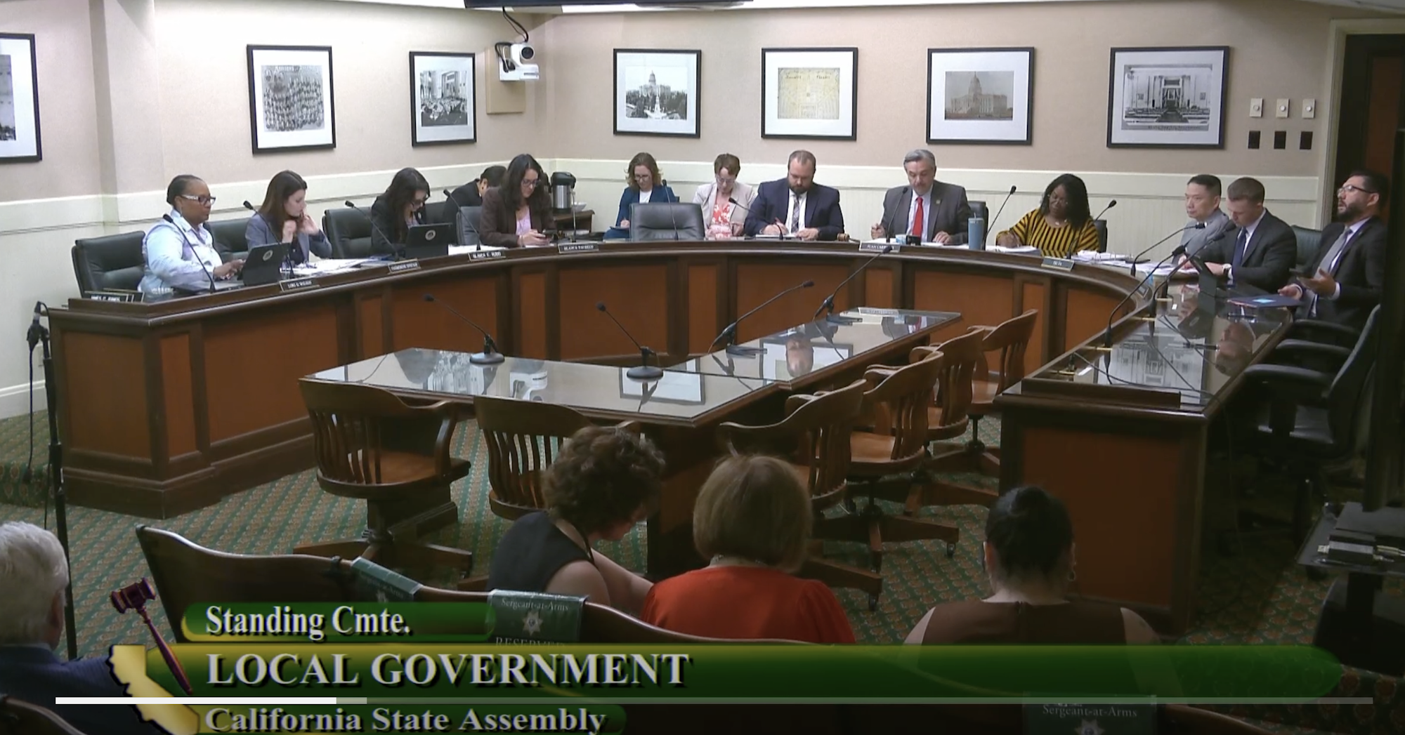 A meeting in a California State Assembly room with officials seated at a large round table.