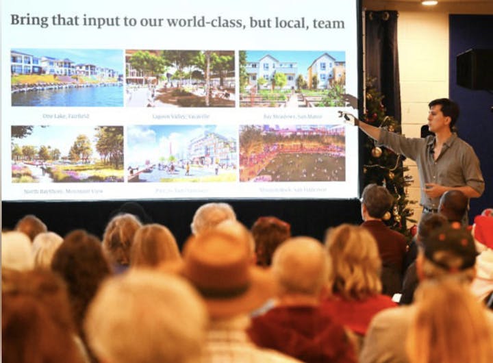 A speaker presents images of various community projects to an audience, emphasizing local input in planning.