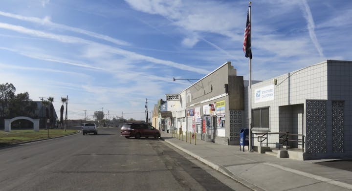 Street view with cars, shops, a flagpole with the US flag, and a clear sky with contrails.