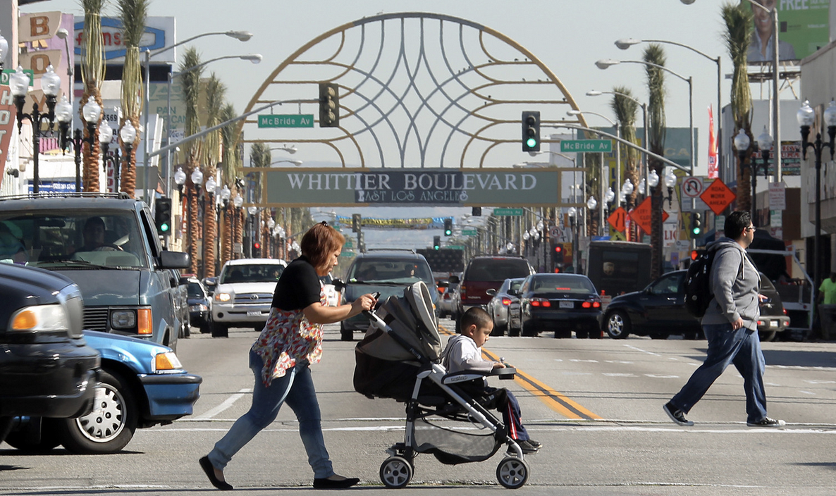 Busy street scene with pedestrians, cars, Whittier Boulevard arch sign in East Los Angeles.
