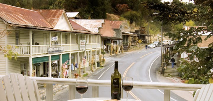 A scenic view of a quaint town with historic buildings, a road, and a table set with wine glasses and a bottle.