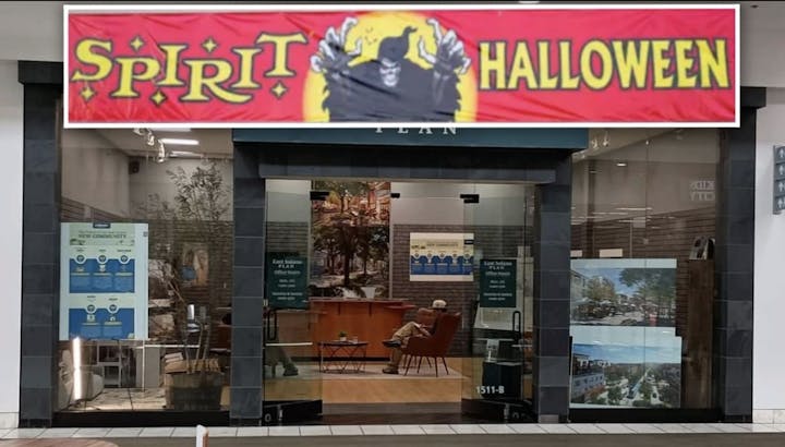 An empty store with a "Spirit Halloween" sign and a person seated inside, possibly in a waiting area.