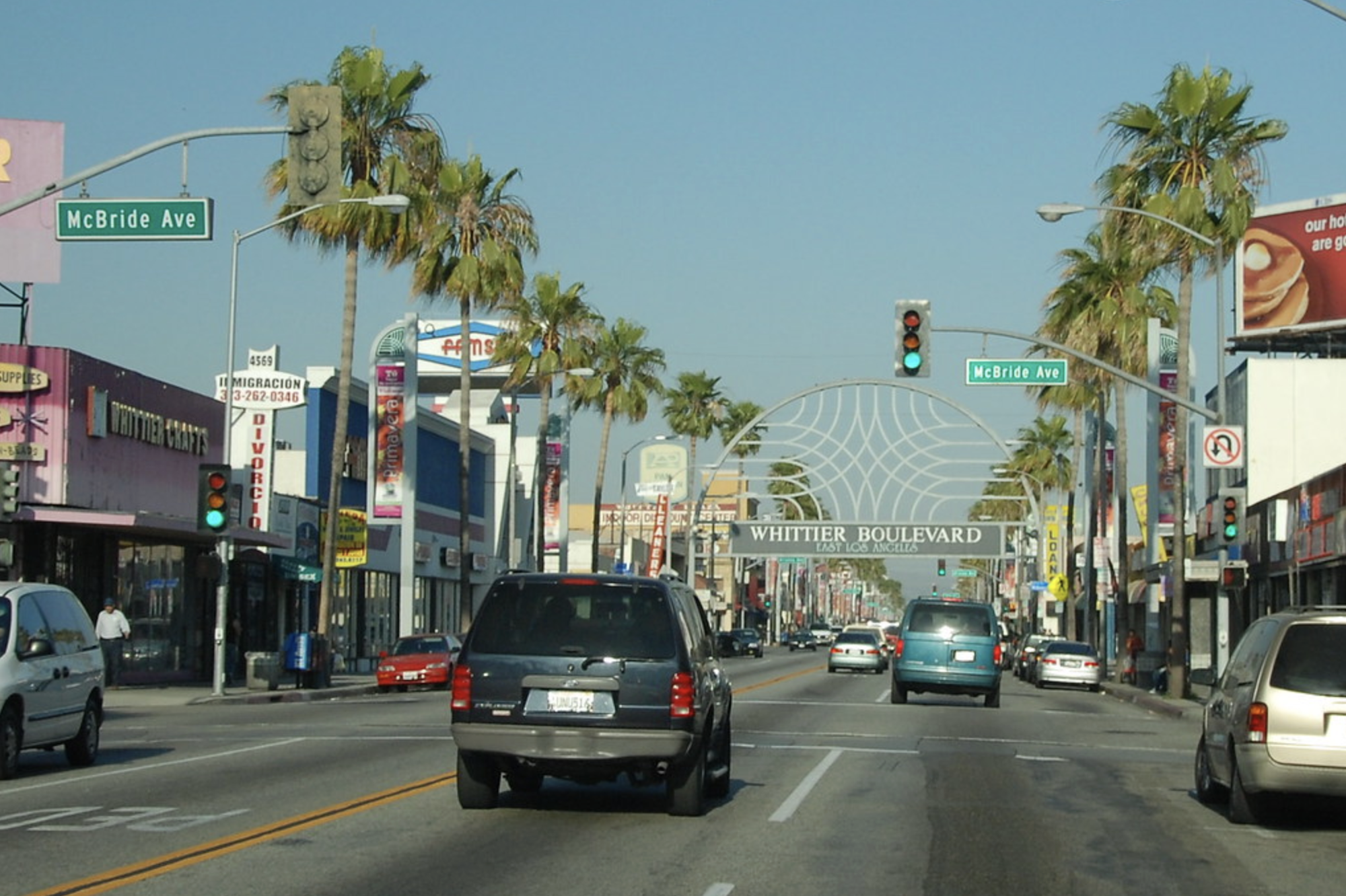 A sunny street scene with cars, palm trees, and a decorative archway saying "Whittier Boulevard East Los Angeles."