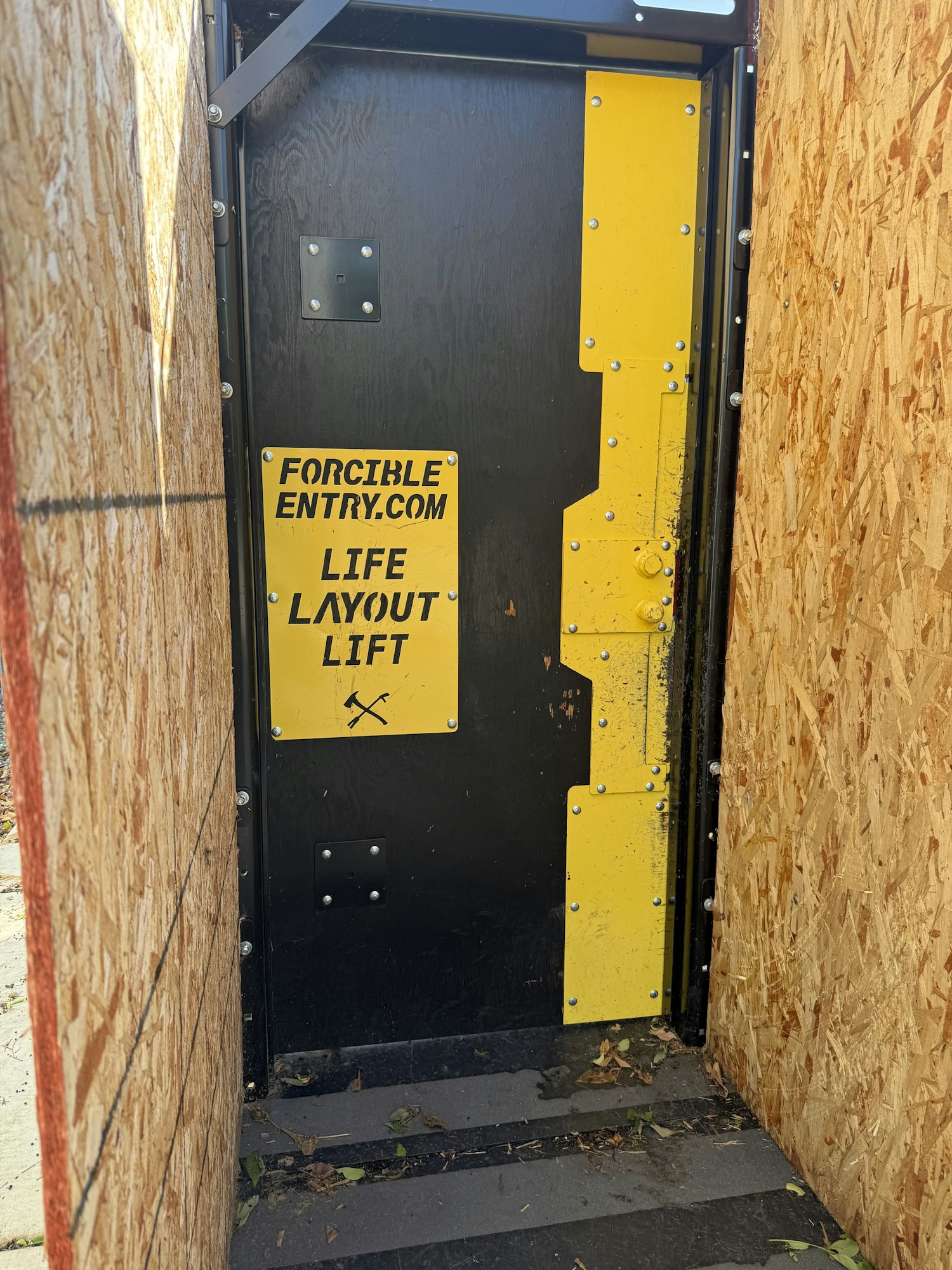 The image shows a black and yellow panel with instructions for a forcible entry and life layout lift, on a wooden structure.