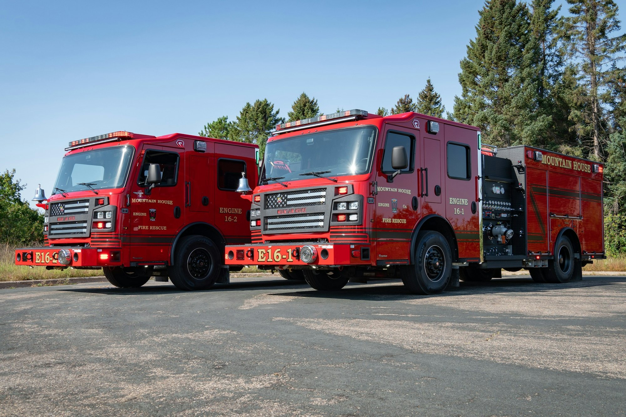 Two red fire trucks labeled "Mountain House," parked on a paved area with trees in the background.