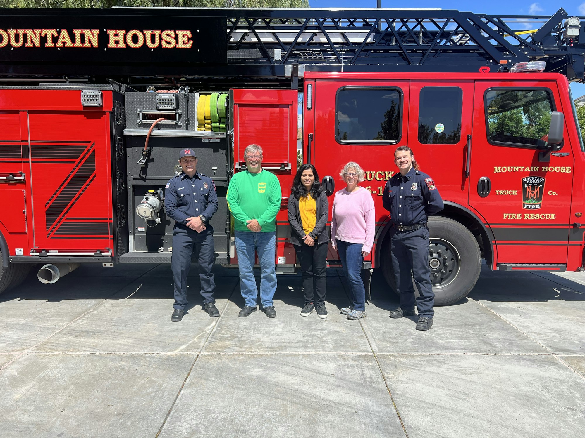 A group of people smiling next to a fire truck labeled "MOUNTAIN HOUSE."