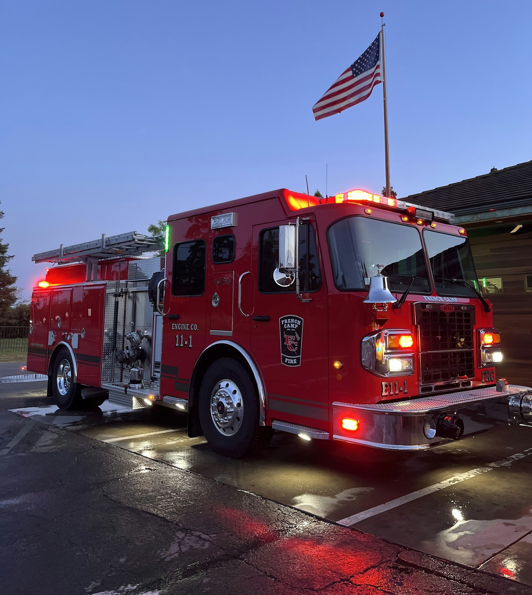 A red fire truck with flashing lights and an American flag in the background.