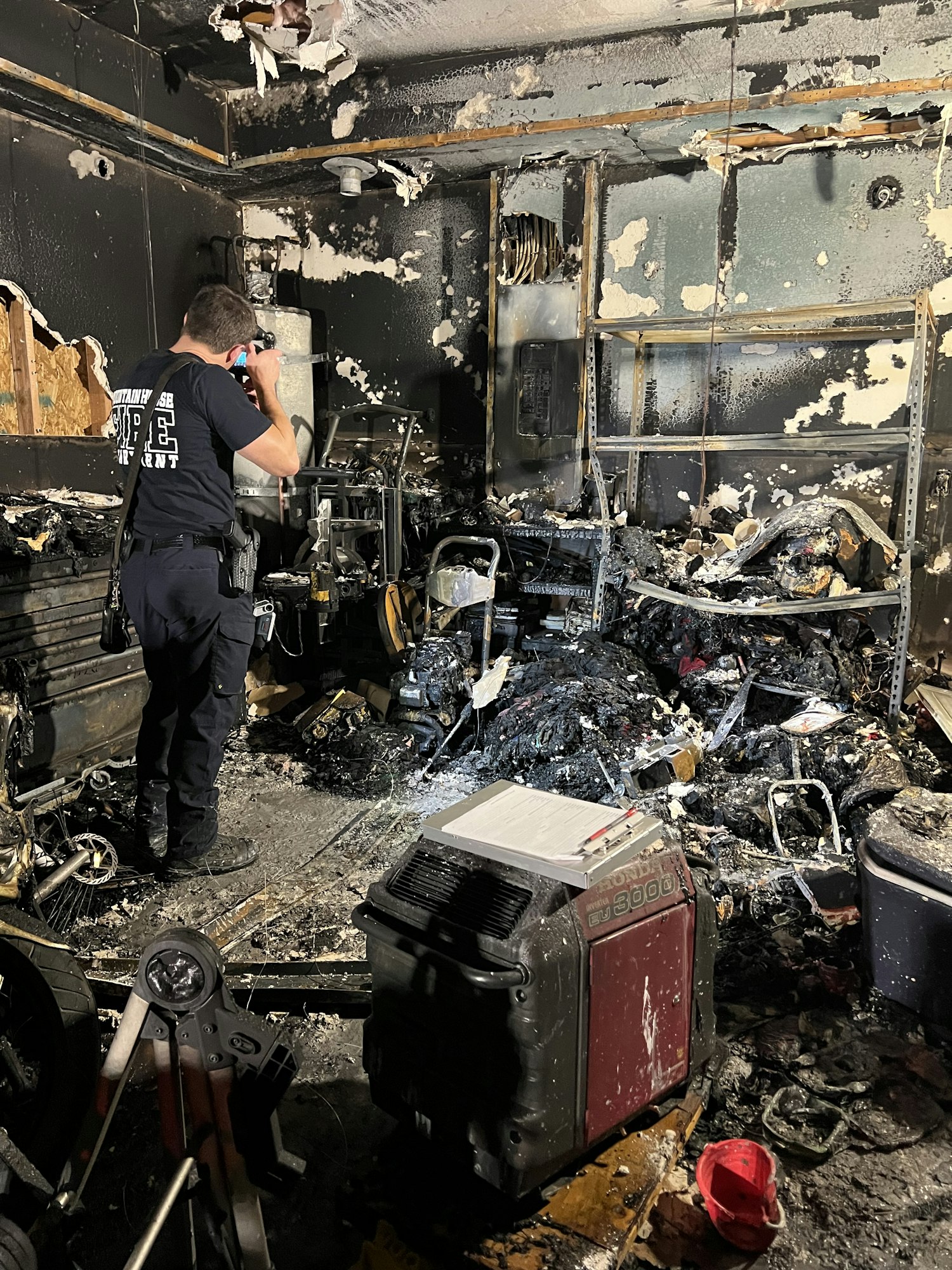 A firefighter inspects a charred room with damaged equipment and debris, aftermath of a fire incident.