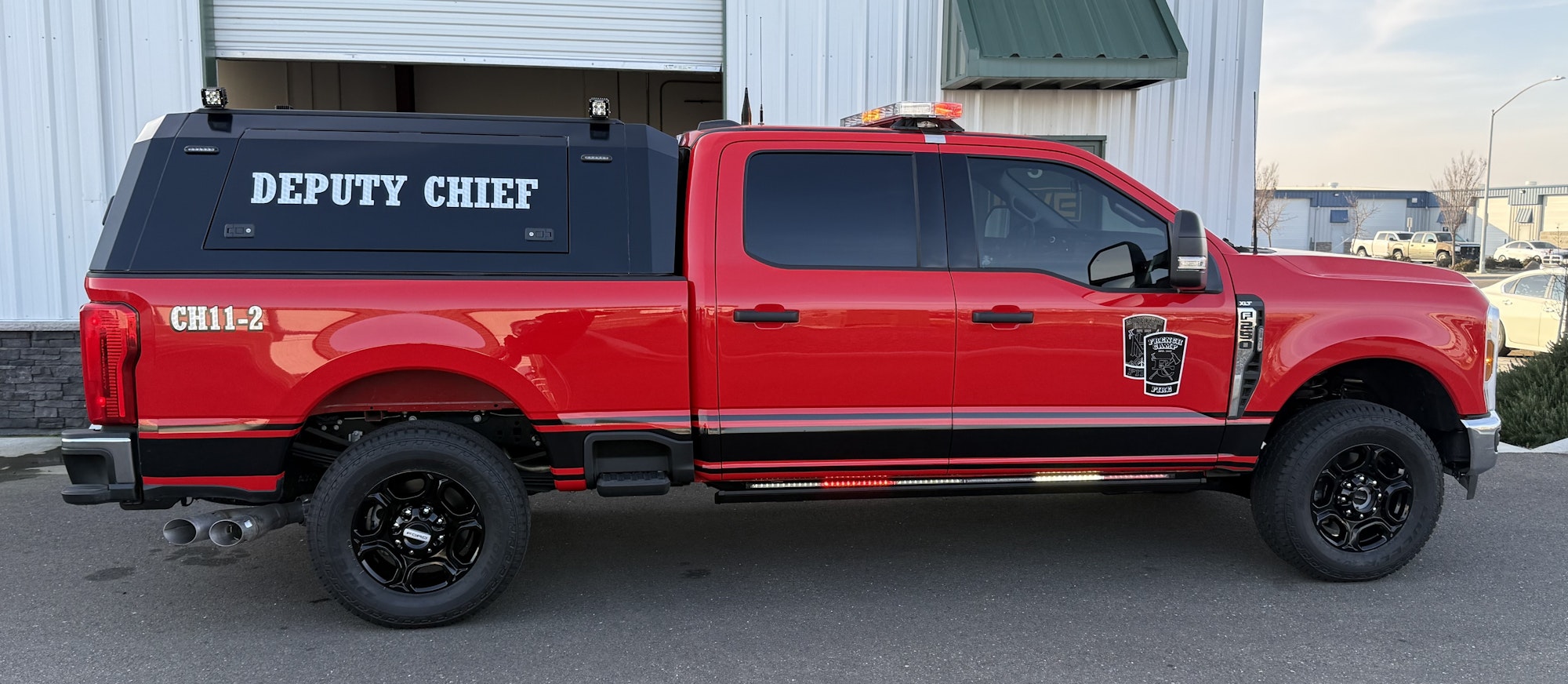 A red truck labeled "DEPUTY CHIEF" with emergency lights and special features, parked near a building.