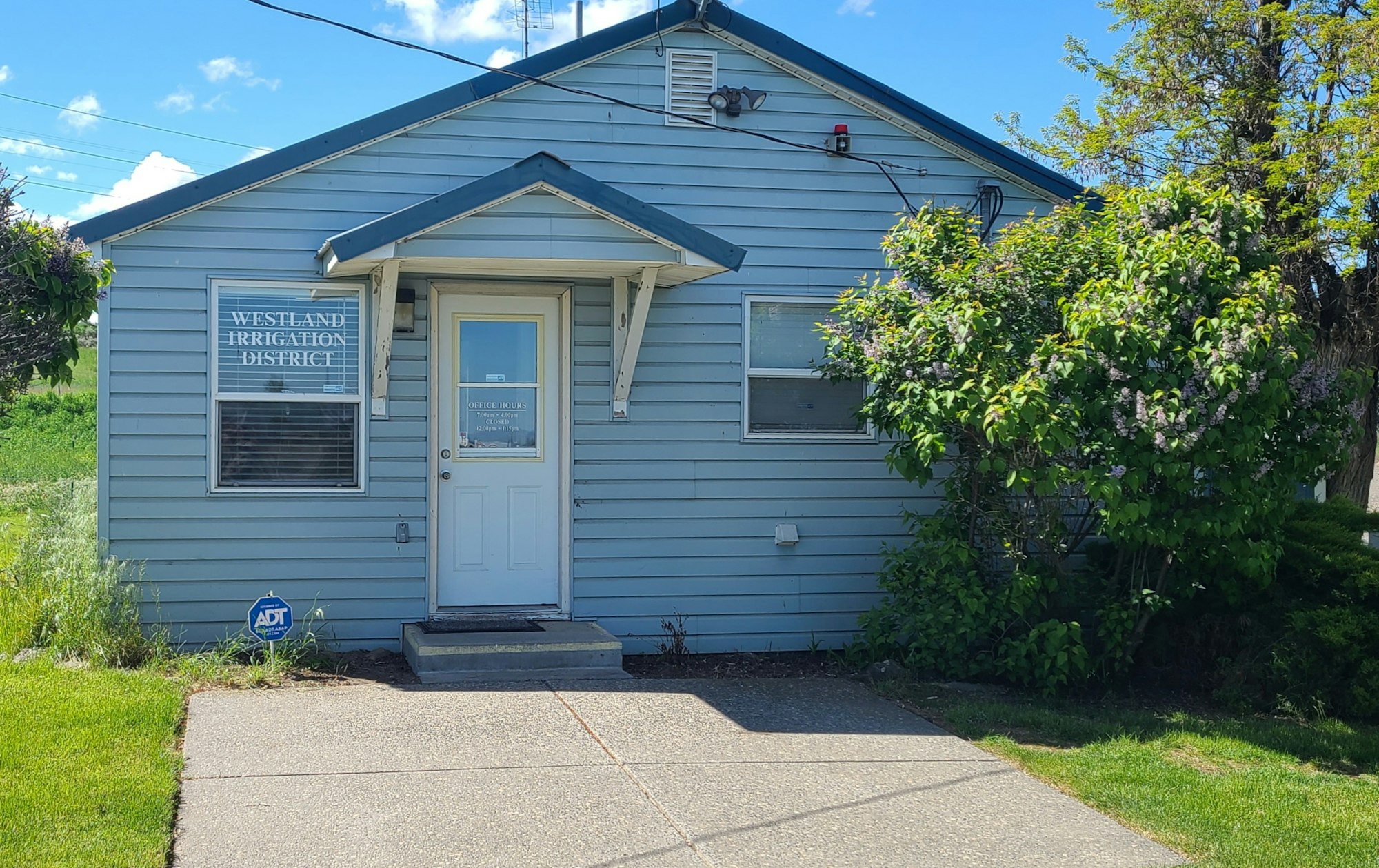 A small blue building with a sign "Westland Irrigation District," surrounded by greenery under a clear sky.