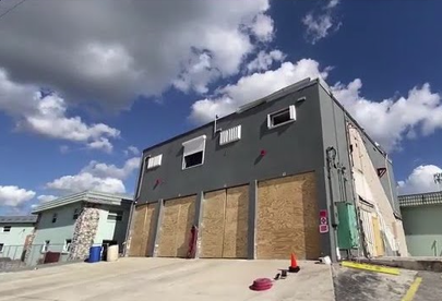 A grey industrial building with boarded windows under a blue sky with clouds.