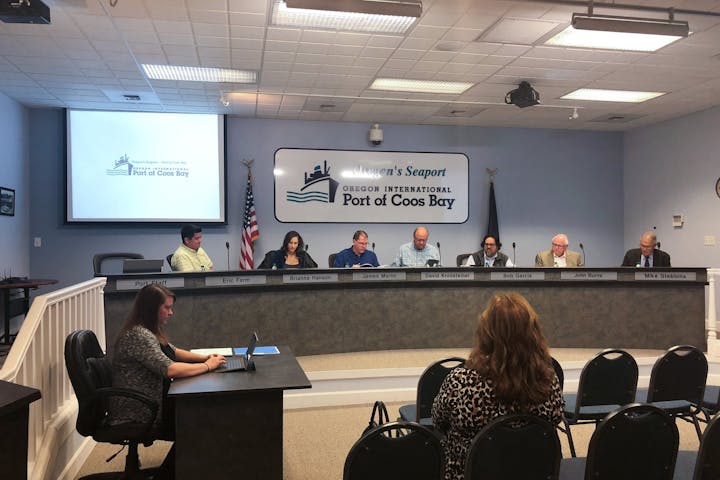 May contain: people, person, adult, female, woman, crowd, flag, electrical device, microphone, desk, furniture, table, computer, electronics, laptop, pc, chair, art, painting, accessories, glasses, bag, handbag, formal wear, tie, and audience