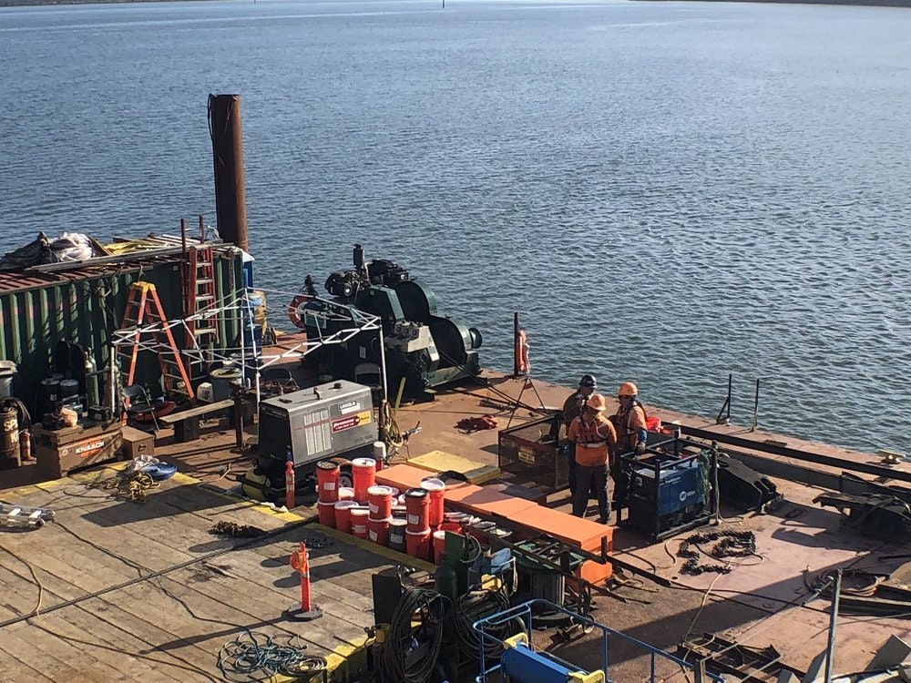 May contain: person, worker, water, waterfront, architecture, building, factory, and helmet