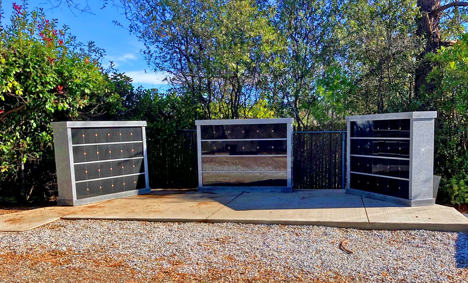 A columbarium with niches surrounded by trees on a sunny day.