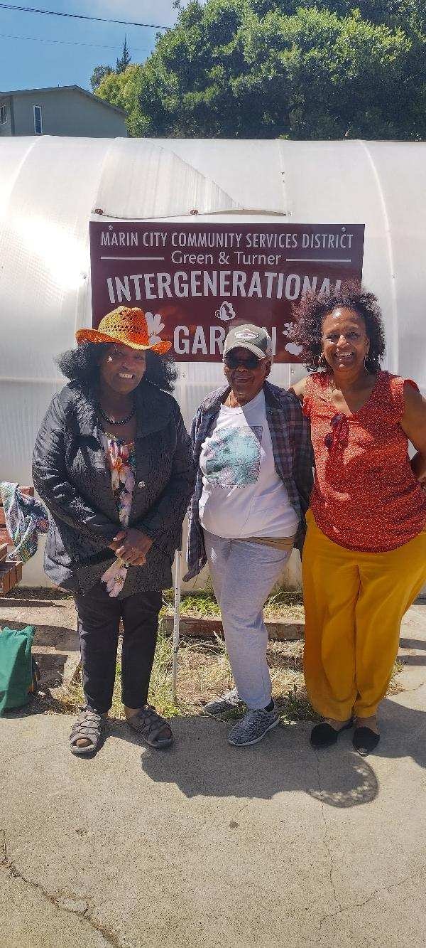Three people smiling in front of a sign that says "Marin City Community Services District Intergenerational Garden."