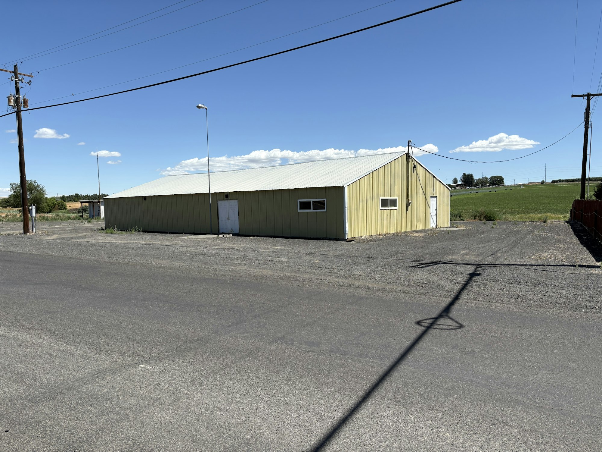 A yellow warehouse-like building with a tin roof, on a rural road, under a clear blue sky.