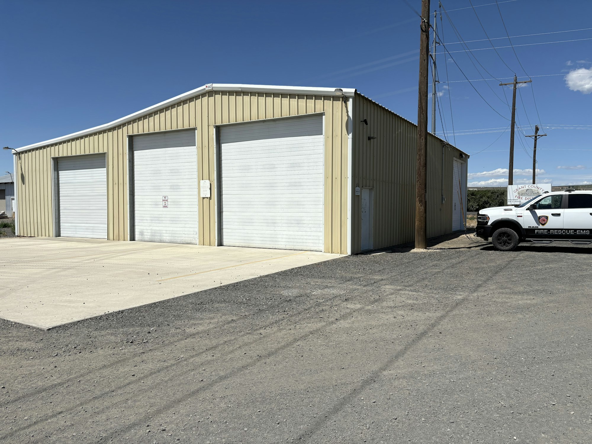 A beige metal building with three large garage doors and a fire-rescue EMS truck parked beside it.