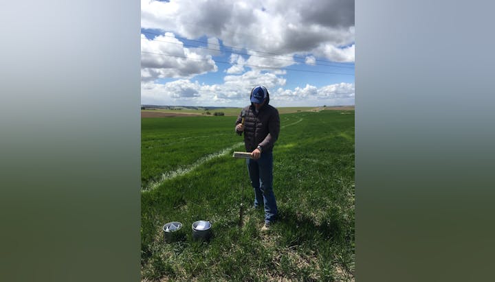 A person conducting a field survey or experiment in a grassy area with equipment, under a cloudy sky.